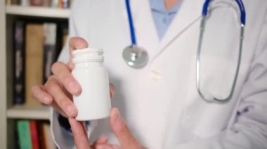 Yakın plan kadın doktor hastanede beyaz önlük giyiyor ve elinde haplar var.