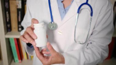 Yakın plan kadın doktor hastanede beyaz önlük giyiyor ve elinde haplar var.
