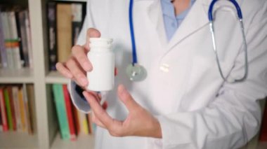 Yakın plan kadın doktor hastanede beyaz önlük giyiyor ve elinde haplar var.