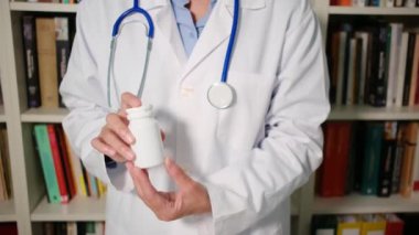 Yakın plan kadın doktor hastanede beyaz önlük giyiyor ve elinde haplar var.