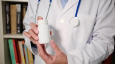 Yakın plan kadın doktor hastanede beyaz önlük giyiyor ve elinde haplar var.