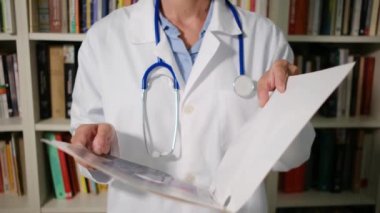 Yakın plan kadın doktor hastanede beyaz önlük giyer ve dosyada belgeler, teşhisler, reçeteler olur.