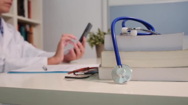 Vista Perto Estetoscópio Com Livros Mesa Médico Feminino Usando Smartphone — Vídeo de Stock