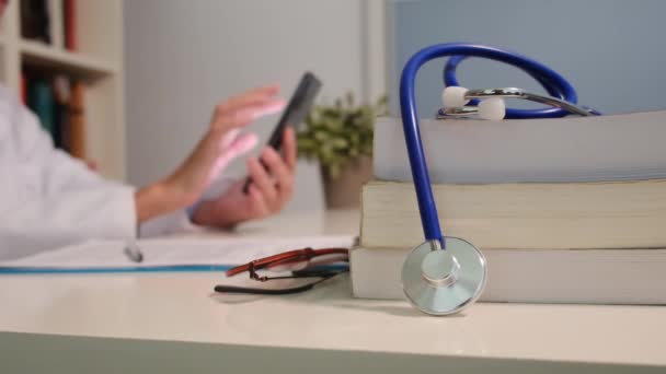 Vista Perto Estetoscópio Com Livros Mesa Médico Feminino Usando Smartphone — Vídeo de Stock
