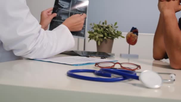 近距离观察身穿白衣的年轻女医生 并与坐在诊所办公桌前的男病人讨论结果或症状 — 图库视频影像