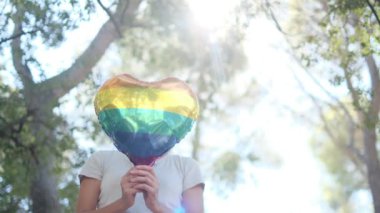Kişi tarafından tutulan LGBTQ + gurur bayrağı renginde kalp şeklinde bir balon. Güneş ışınları eşitliği, cinsel özgürlüğü, cinsiyet saygısını ve dahil edilmeyi simgeliyor.