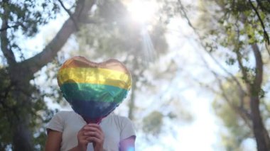 Kişi tarafından tutulan LGBTQ + gurur bayrağı renginde kalp şeklinde bir balon. Güneş ışınları eşitliği, cinsel özgürlüğü, cinsiyet saygısını ve dahil edilmeyi simgeliyor.