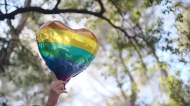 Kişi tarafından tutulan LGBTQ + gurur bayrağı renginde kalp şeklinde bir balon. Güneş ışınları eşitliği, cinsel özgürlüğü, cinsiyet saygısını ve dahil edilmeyi simgeliyor.