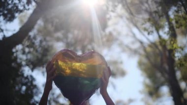 Kişi tarafından tutulan LGBTQ + gurur bayrağı renginde kalp şeklinde bir balon. Güneş ışınları eşitliği, cinsel özgürlüğü, cinsiyet saygısını ve dahil edilmeyi simgeliyor.