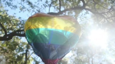 Kişi tarafından tutulan LGBTQ + gurur bayrağı renginde kalp şeklinde bir balon. Güneş ışınları eşitliği, cinsel özgürlüğü, cinsiyet saygısını ve dahil edilmeyi simgeliyor.