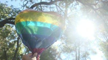 Kişi tarafından tutulan LGBTQ + gurur bayrağı renginde kalp şeklinde bir balon. Güneş ışınları eşitliği, cinsel özgürlüğü, cinsiyet saygısını ve dahil edilmeyi simgeliyor.
