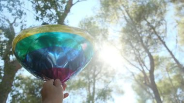 Kişi tarafından tutulan LGBTQ + gurur bayrağı renginde kalp şeklinde bir balon. Güneş ışınları eşitliği, cinsel özgürlüğü, cinsiyet saygısını ve dahil edilmeyi simgeliyor.