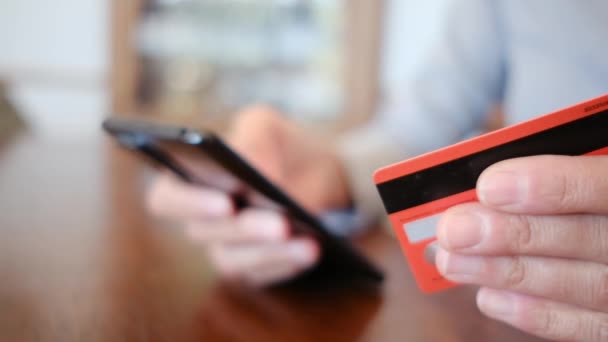 スマートフォンやクレジットカードを持ち 自宅でオンラインショッピングをする女性の手のクローズアップ オンラインショッピング ライフスタイルの概念 — ストック動画