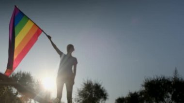 Gün batımında dalgalanan LGBTQ + bayrağıyla yalnız genç bir kadın. Eşitlik, eşitlik, dahil etme, LGBTQ konsepti. Aşk aşktır, ayrımcılık yok, özgürlüğe evet