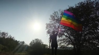 Gün batımında dalgalanan LGBTQ + bayrağıyla yalnız genç bir kadın. Eşitlik, eşitlik, dahil etme, LGBTQ konsepti. Aşk aşktır, ayrımcılık yok, özgürlüğe evet