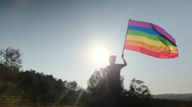 Gün batımında dalgalanan LGBTQ + bayrağıyla yalnız genç bir kadın. Eşitlik, eşitlik, dahil etme, LGBTQ konsepti. Aşk aşktır, ayrımcılık yok, özgürlüğe evet