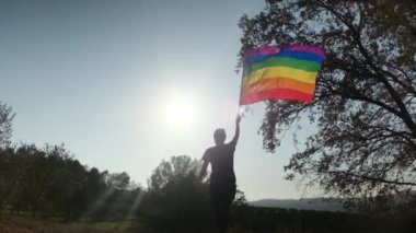 Gün batımında dalgalanan LGBTQ + bayrağıyla yalnız genç bir kadın. Eşitlik, eşitlik, dahil etme, LGBTQ konsepti. Aşk aşktır, ayrımcılık yok, özgürlüğe evet
