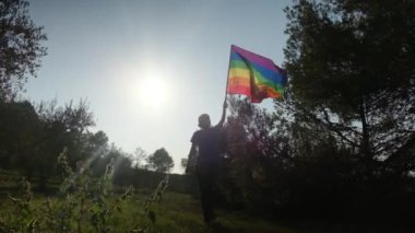 Gün batımında dalgalanan LGBTQ + bayrağıyla yalnız genç bir kadın. Eşitlik, eşitlik, dahil etme, LGBTQ konsepti. Aşk aşktır, ayrımcılık yok, özgürlüğe evet