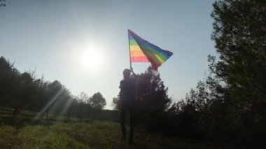 Gün batımında dalgalanan LGBTQ + bayrağıyla yalnız genç bir kadın. Eşitlik, eşitlik, dahil etme, LGBTQ konsepti. Aşk aşktır, ayrımcılık yok, özgürlüğe evet