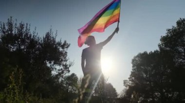 Gün batımında dalgalanan LGBTQ + bayrağıyla yalnız genç bir kadın. Eşitlik, eşitlik, dahil etme, LGBTQ konsepti. Aşk aşktır, ayrımcılık yok, özgürlüğe evet