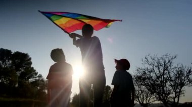Anne ve iki çocuk gün batımında bir dağın tepesinde LGBTQ + bayrağı sallıyorlar. Aile, çeşitlilik, kapsama ve eşitlik kavramı. Gurur, lezbiyen anne ve çocuklar. Aşk aşktır.