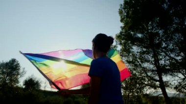 Gün batımında elinde lgbt bayrağı olan kadın silueti