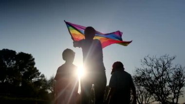 Anne ve iki çocuk gün batımında bir dağın tepesinde LGBTQ + bayrağı sallıyorlar. Aile, çeşitlilik, kapsama ve eşitlik kavramı. Gurur, lezbiyen anne ve çocuklar. Aşk aşktır.