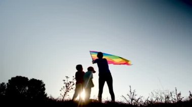 Anne ve iki çocuk gün batımında bir dağın tepesinde LGBTQ + bayrağı sallıyorlar. Aile, çeşitlilik, kapsama ve eşitlik kavramı. Gurur, lezbiyen anne ve çocuklar. Aşk aşktır.