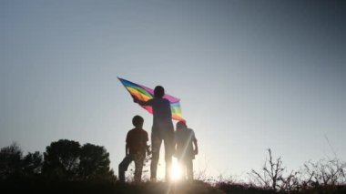 Anne ve iki çocuk gün batımında bir dağın tepesinde LGBTQ + bayrağı sallıyorlar. Aile, çeşitlilik, kapsama ve eşitlik kavramı. Gurur, lezbiyen anne ve çocuklar. Aşk aşktır.