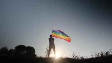 Gün batımında dalgalanan LGBTQ + bayrağıyla yalnız genç bir kadın. Eşitlik, eşitlik, dahil etme, LGBTQ konsepti. Aşk aşktır, ayrımcılık yok, özgürlüğe evet