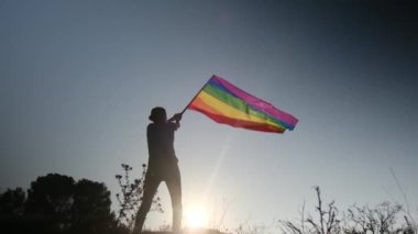 Gün batımında dalgalanan LGBTQ + bayrağıyla yalnız genç bir kadın. Eşitlik, eşitlik, dahil etme, LGBTQ konsepti. Aşk aşktır, ayrımcılık yok, özgürlüğe evet