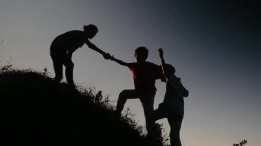 Bir annenin siluetleri oğullarının tepeye tırmanmasına yardım ediyor. 