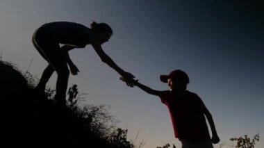 Bir annenin silueti oğlunun tepeye tırmanmasına yardım ediyor. 