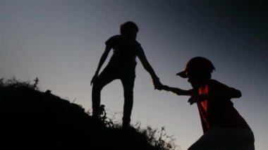 Bir annenin silueti oğlunun tepeye tırmanmasına yardım ediyor. 