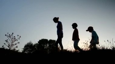 Anne ve çocuklar gün batımında tepede yürüyor. 