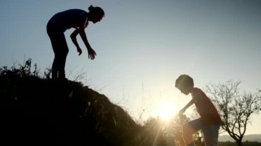 Bir annenin silueti oğlunun tepeye tırmanmasına yardım ediyor. 