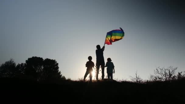 母と2人の子供が日没時に山の上にLgbtq 旗を掲げています 多様性 平等という概念 レズビアンの母親 そして子供たち — ストック動画