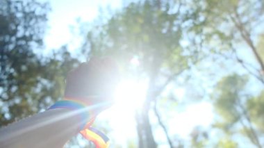 Gökkuşağı renkli LGBT bileklikle el ve yumruk havada. Gurur, eşitlik, eşitlik kavramı. Güneşli bir günde gökyüzüne yumruk ve güneş ışığı yansıması. Eşitlik, kapsama, ayrımcılık yok, kabul