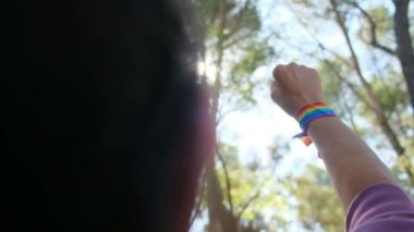 Gökkuşağı renkli LGBT bileklikle el ve yumruk havada. Gurur, eşitlik, eşitlik kavramı. Güneşli bir günde gökyüzüne yumruk ve güneş ışığı yansıması. Eşitlik, kapsama, ayrımcılık yok, kabul