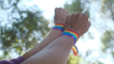 Gökkuşağı renkli LGBT bileklikle eller ve yumruklar havaya. Gurur, eşitlik, eşitlik kavramı. Güneşli bir günde gökyüzüne yumruk ve güneş ışığı yansıması. Eşitlik, kapsama, ayrımcılık yok, kabul