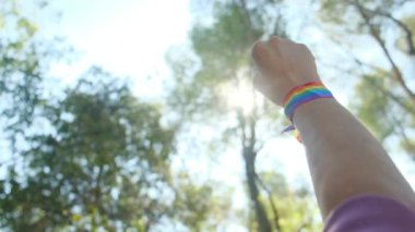 Gökkuşağı renkli LGBT bileklikle el ve yumruk havada. Gurur, eşitlik, eşitlik kavramı. Güneşli bir günde gökyüzüne yumruk ve güneş ışığı yansıması. Eşitlik, kapsama, ayrımcılık yok, kabul