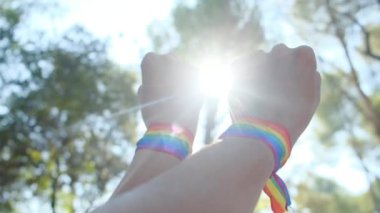 Gökkuşağı renkli LGBT bileklikle eller ve yumruklar havaya. Gurur, eşitlik, eşitlik kavramı. Güneşli bir günde gökyüzüne yumruk ve güneş ışığı yansıması. Eşitlik, kapsama, ayrımcılık yok, kabul
