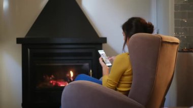 Akıllı telefonlu kadın şöminenin yanında.