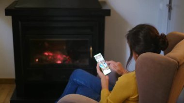 Sıcak çoraplı, şöminenin yanında akıllı telefonu olan bir kadın.