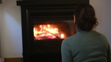 Kadın şöminenin yanında ellerini ısıtıyor.