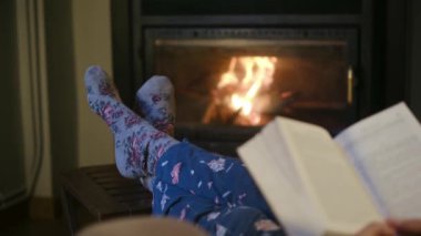 Şöminenin yanında kitap okuyan kadın.