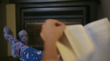 Şöminenin yanında kitap okuyan kadın.