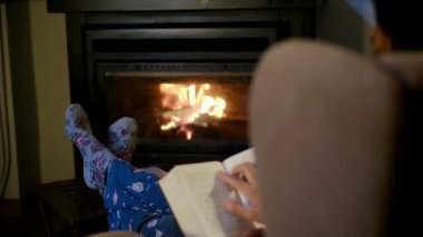 Şöminenin yanında kitap okuyan kadın.