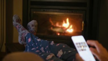 Sıcak çoraplı, şöminenin yanında akıllı telefonu olan bir kadın.