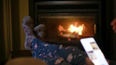 Sıcak çoraplı, şöminenin yanında akıllı telefonu olan bir kadın.
